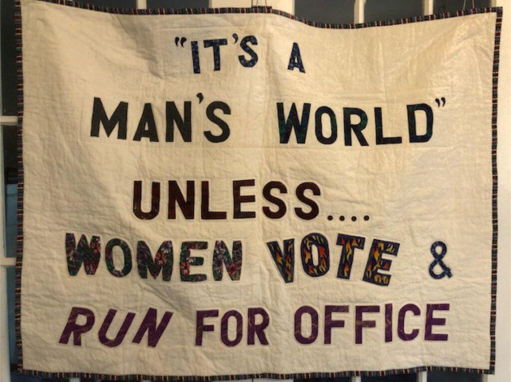 Photo of Phyllis Maddox’s quilt provided the backing for our new precinct map.  It reads: "It's a man's world unless... women vote & run for office"